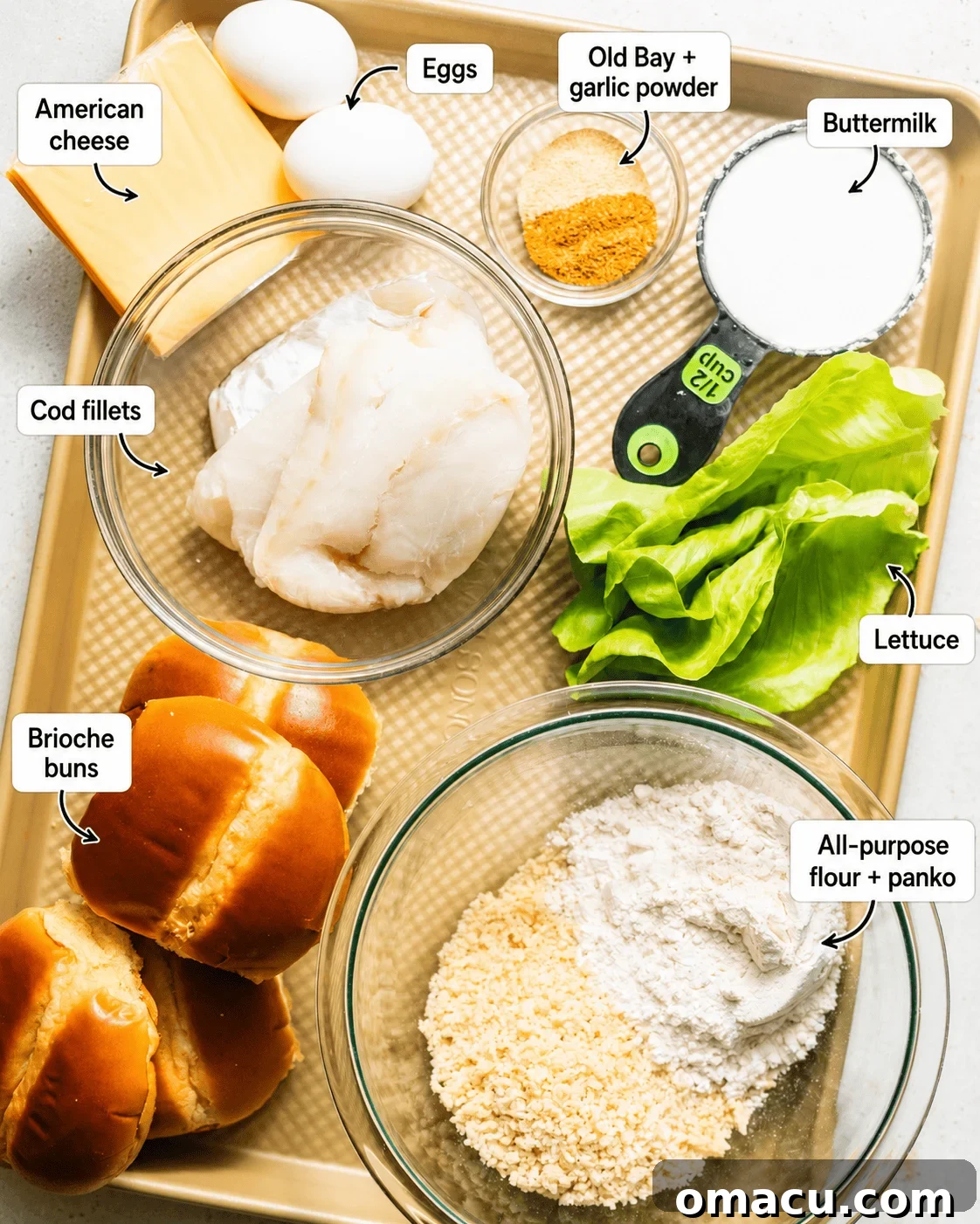 ingredients to make fried fish sandwiches on a baking sheet - cod, american cheese, lettuce, brioche buns, buttermilk, eggs, panko breadcrumbs, flour, and seasonings.