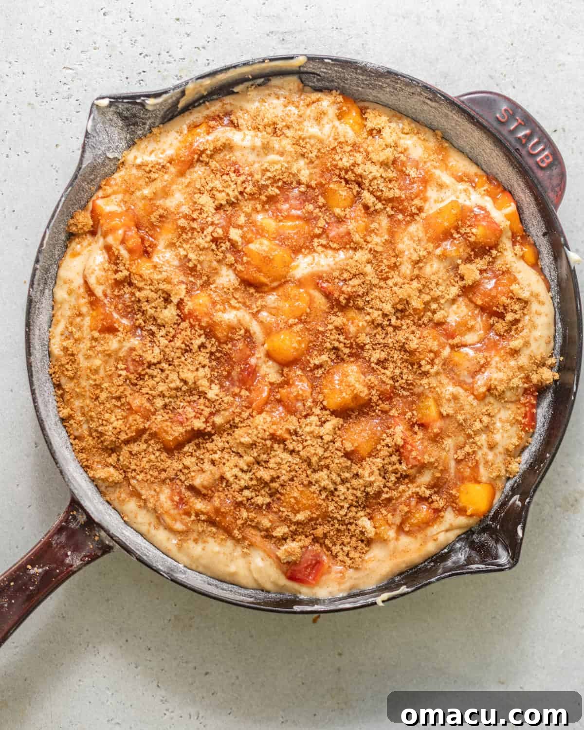 Skillet Peach Fritter Cake with Vanilla Bean Glaze 6 cake batter in a skillet with peach filling swirled throughout and topped with a brown sugar crunch topping.