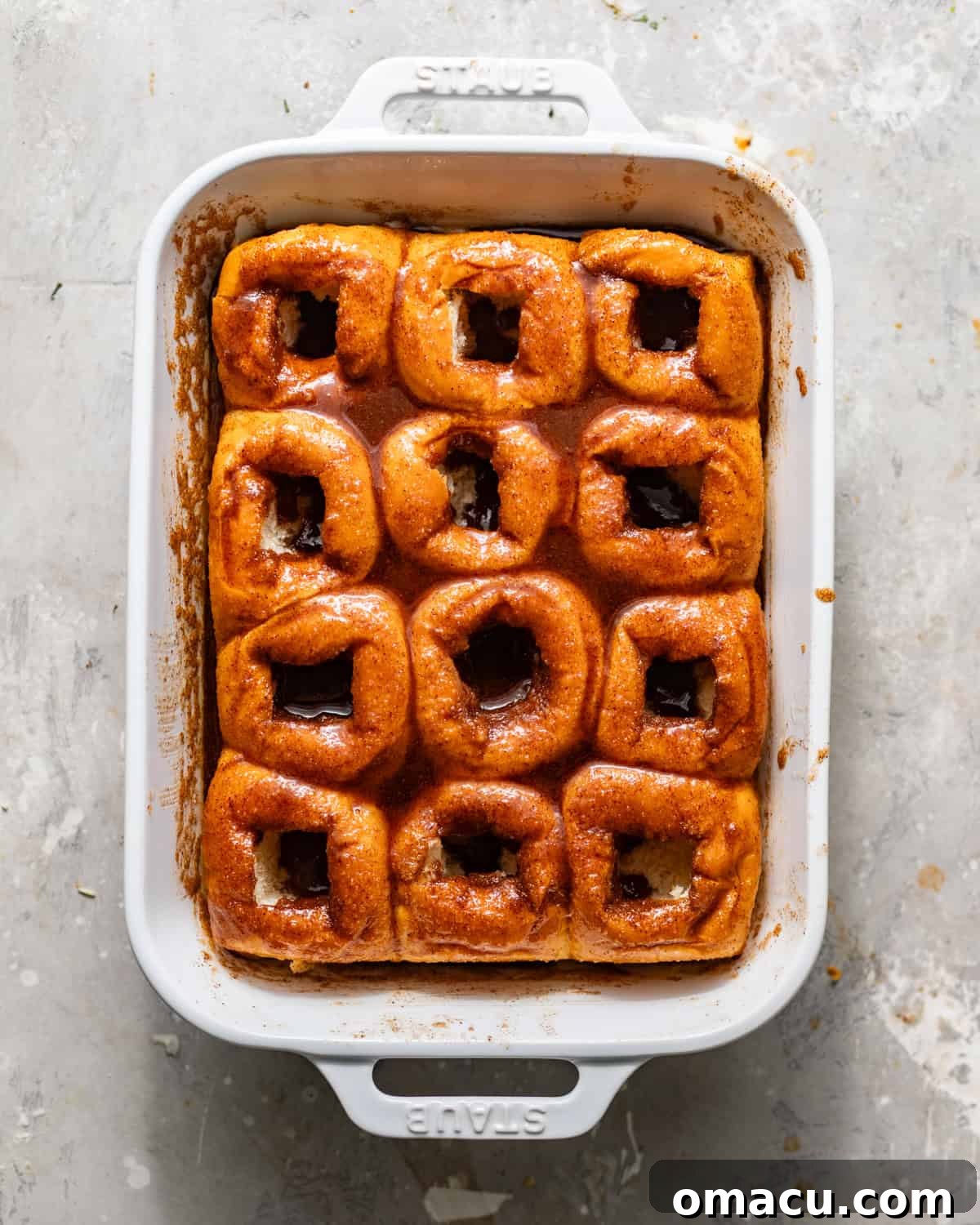 hawaiian rolls in a baking dish with the center of the rolls cut out and covered in cinnamon roll filling.