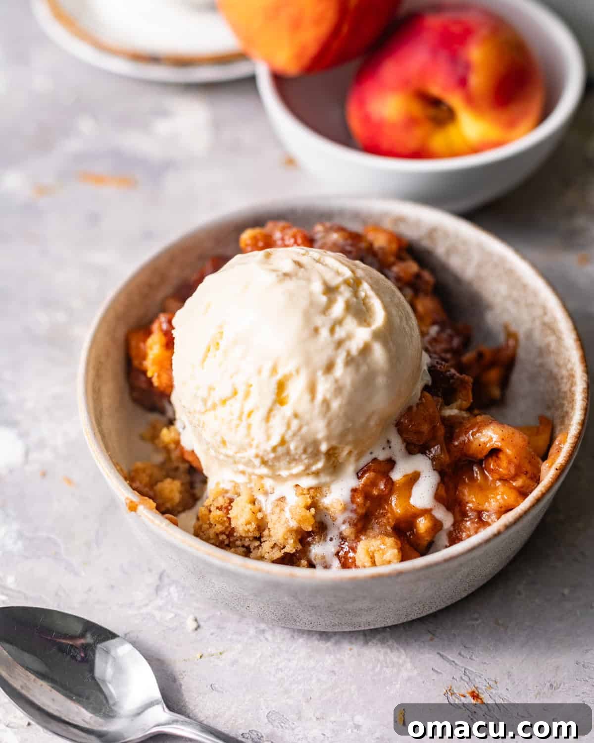 peach cobbler cinnamon roll bites in a bowl topped with ice cream.