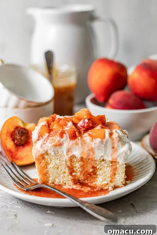 a slice of peach cobbler tres leches on a plate topped with whipped cream, cooked peaches, and peach syrup.