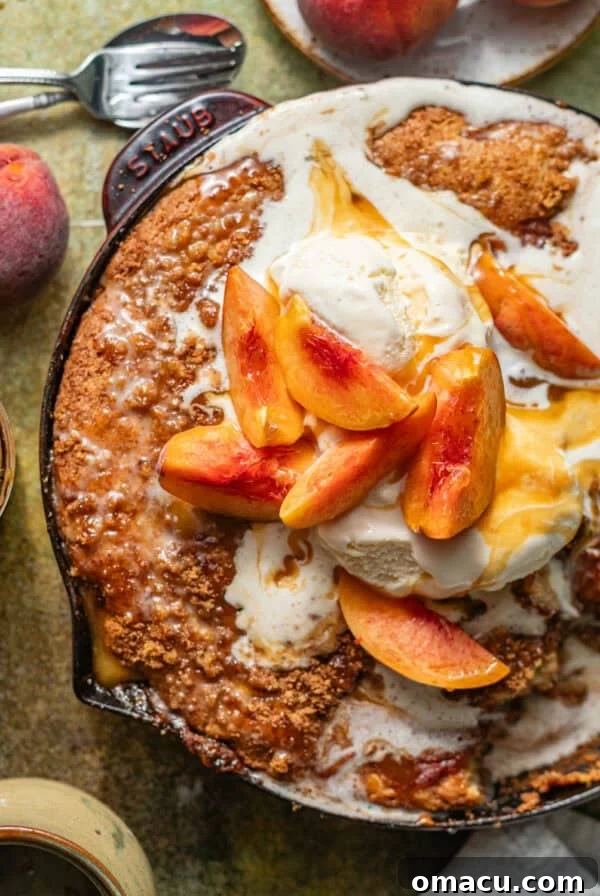 peach fritter cake in a skillet topped with ice cream and fresh peaches.