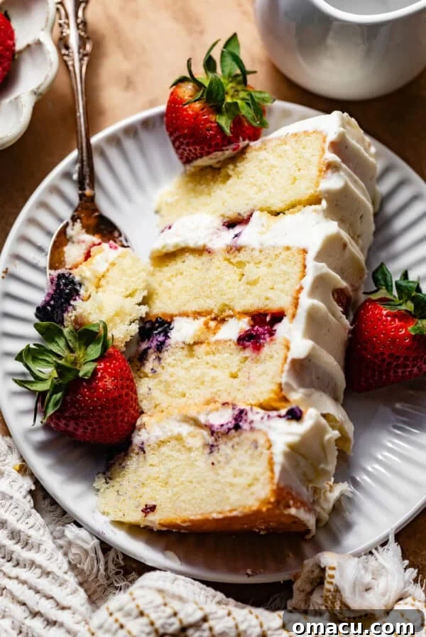 a slice of berry chantilly cake on a plate with fresh berries and a fork.