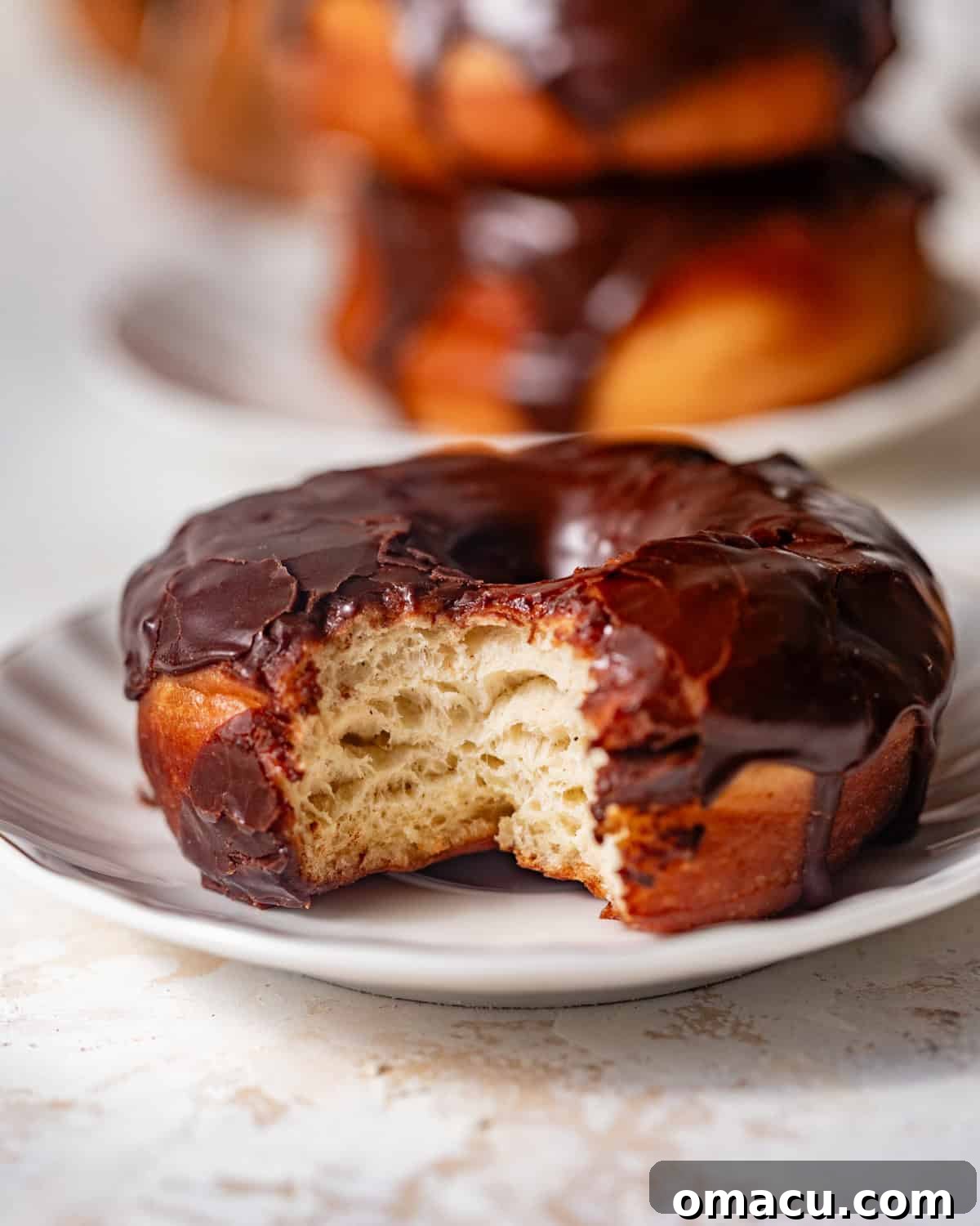Chocolate glazed donut on a plate with a bite taken out, showing the soft interior.