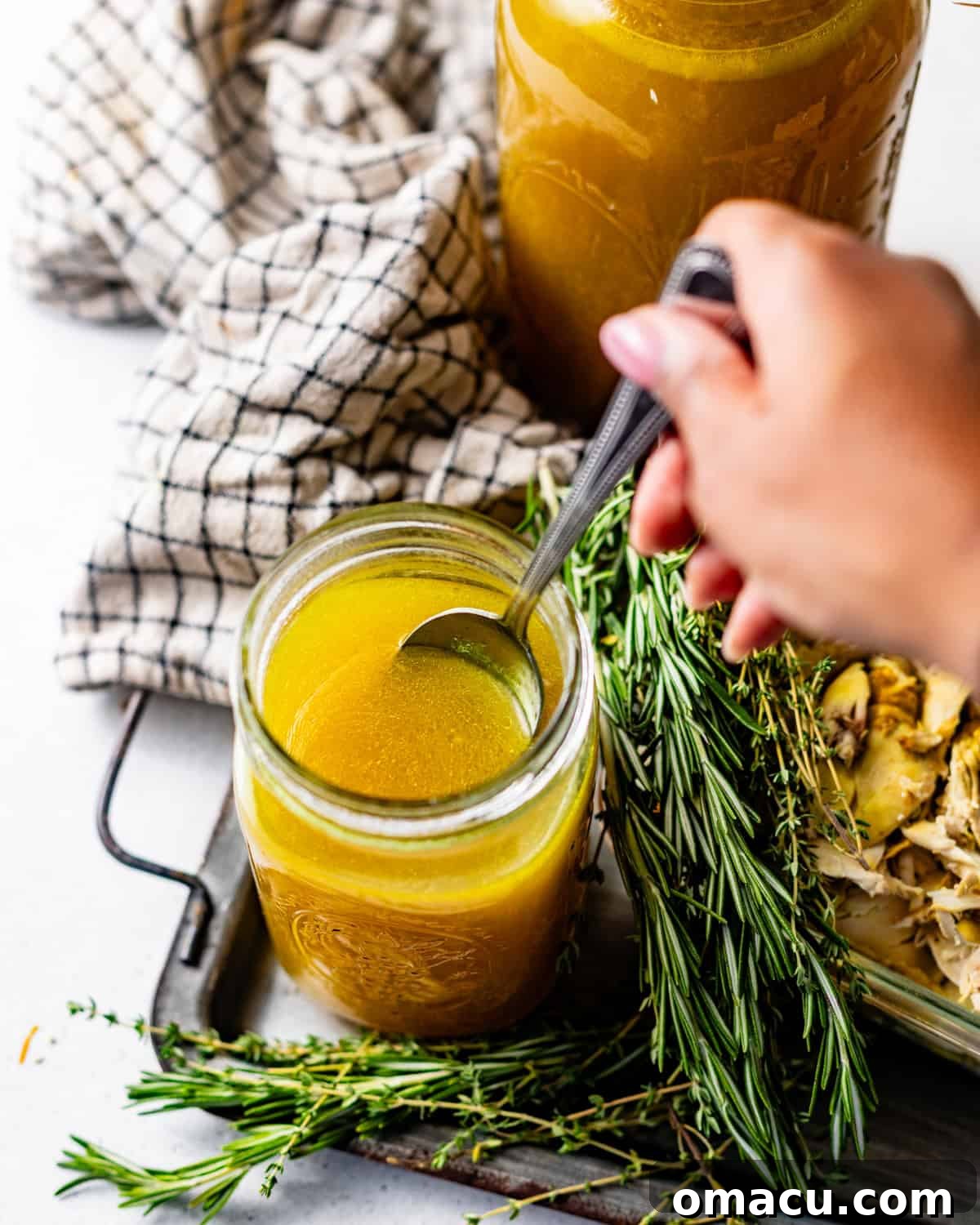 a hand using a spoon to scoop the chicken broth out of the jar.
