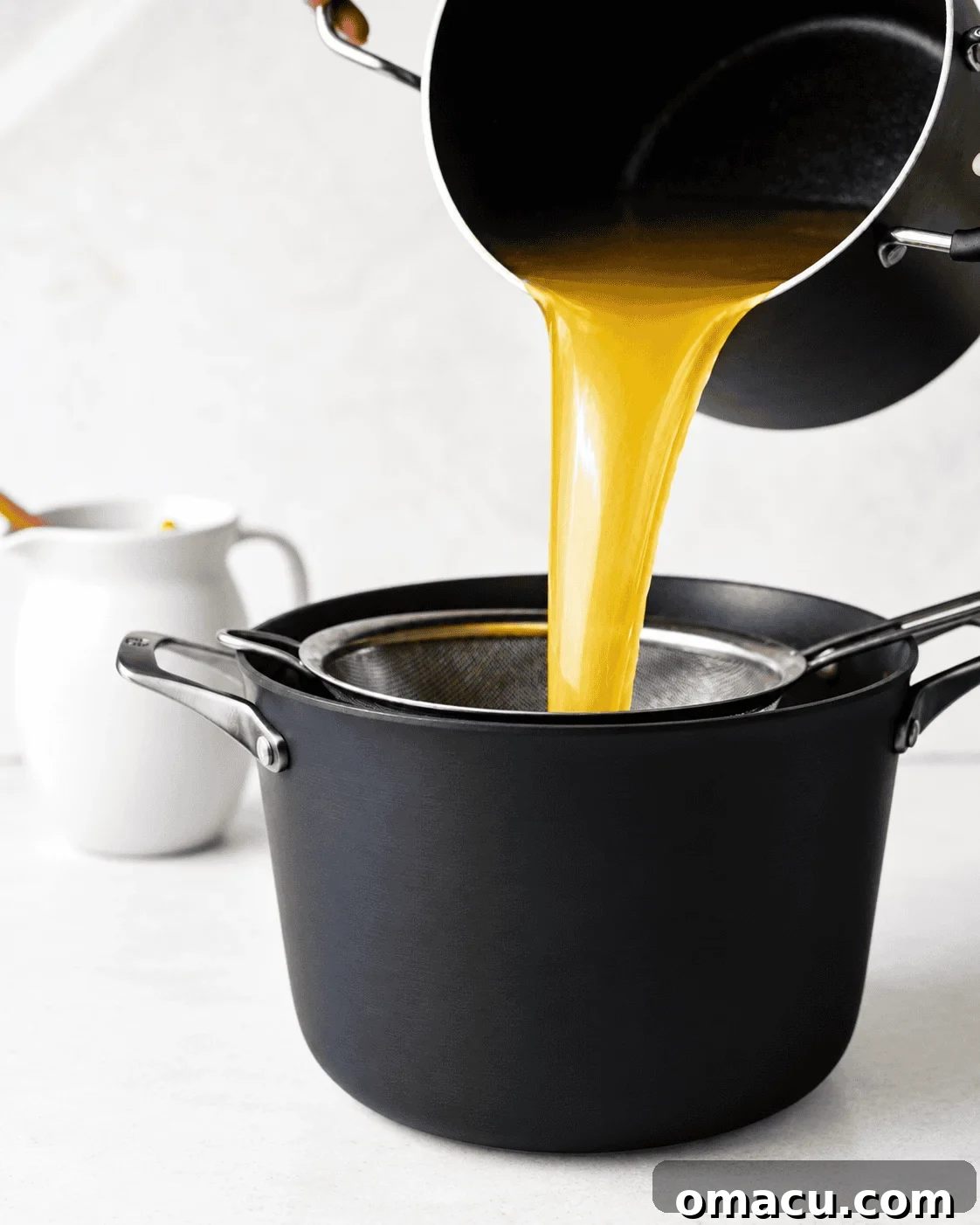 Homemade chicken broth being poured through a fine-mesh strainer into a large pot.