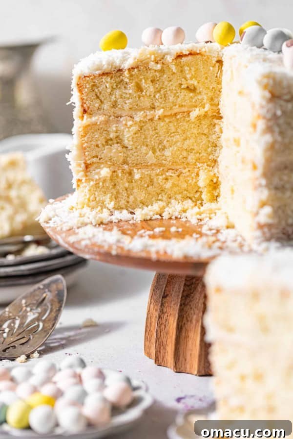 coconut cake on a cake stand topped with mini eggs and coated in coconut shreds.