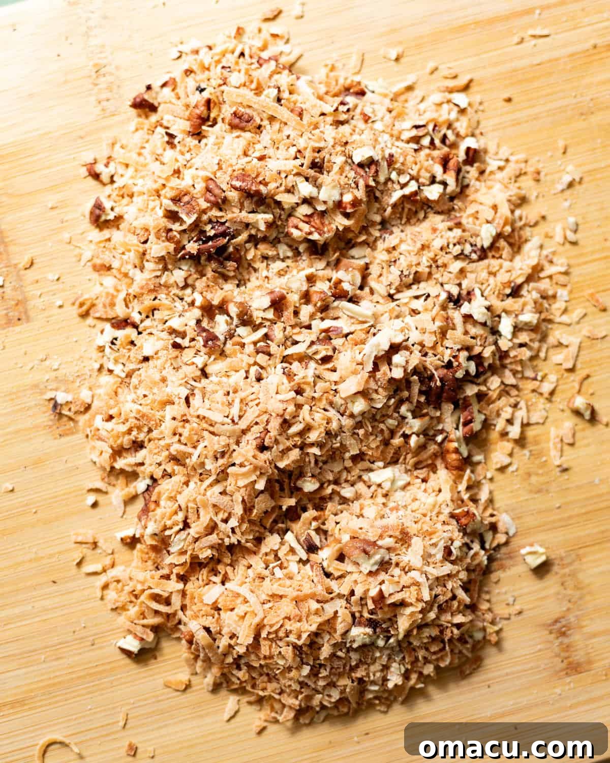Classic Italian Cream Cake Recipe with Cream Cheese Frosting 5 Finely chopped toasted coconut and pecans on a wooden cutting board.