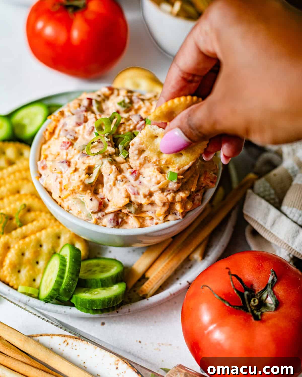 Creamy Southern Pimento Cheese Dip for Game Day 5 a hand dipping crackers into a bowl of pimento cheese.
