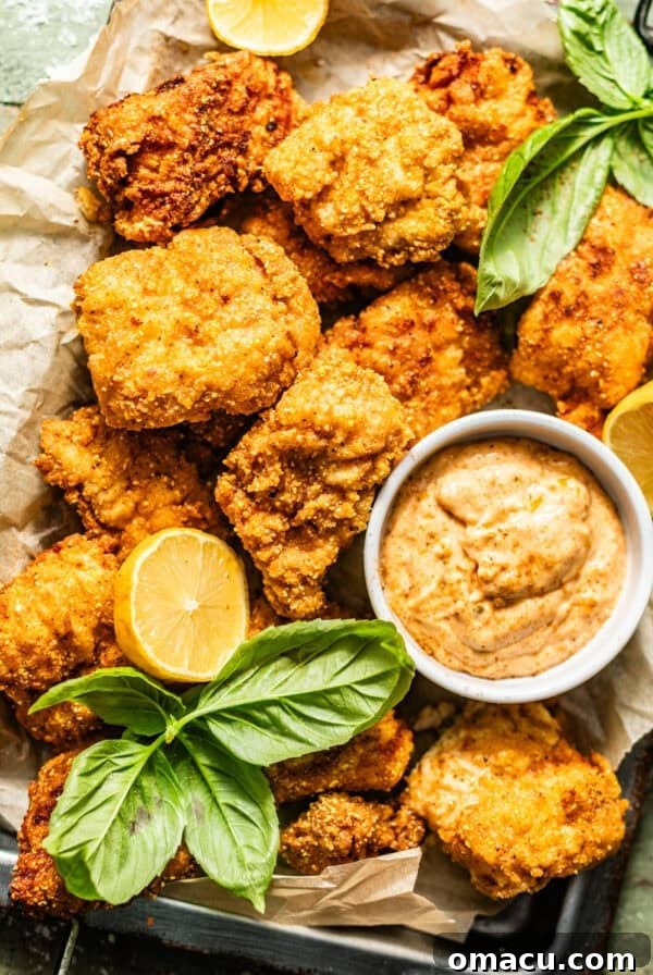 crispy catfish nuggets on a serving tray with Cajun tartar sauce with lemon wedges and fresh herbs on top for garnish.