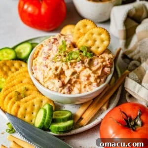 Creamy Southern Pimento Cheese Dip for Game Day 10 pimento cheese in a bowl surrounded by crackers, sliced cucumbers, and breadsticks.