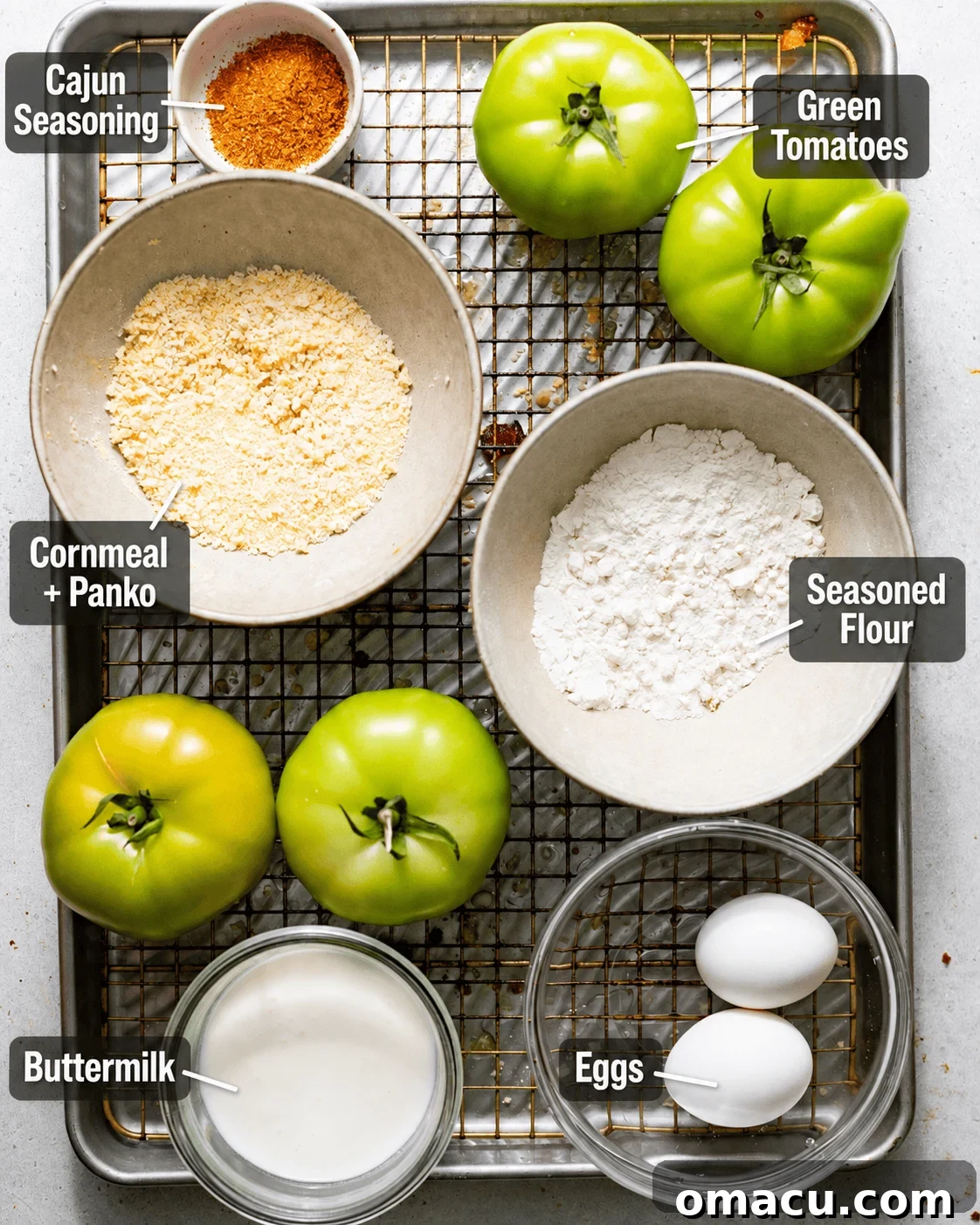 Crispy Southern Fried Green Tomatoes Recipe 3 ingredients to make fried green tomatoes on a baking sheet - sliced green tomatoes, Cajun seasoning, flour, panko breadcrumbs, cornmeal, buttermilk, and eggs