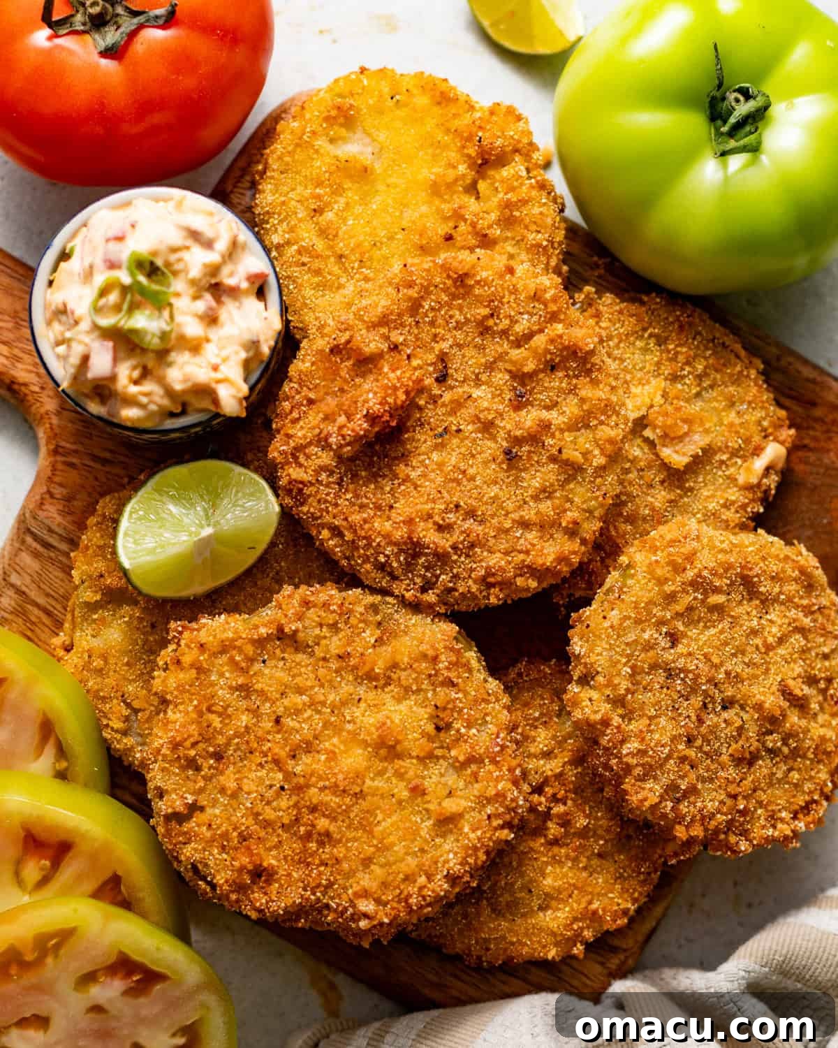 Crispy Southern Fried Green Tomatoes Recipe 9 fried green tomatoes on a serving board with a small bowl of pimento cheese and a lime wedge on the side.