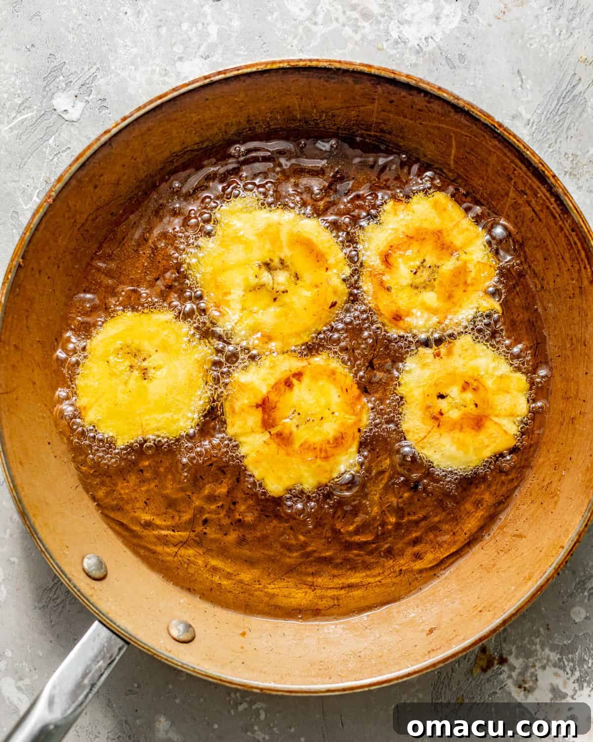 Crispy Tostones Recipe: Authentic Fried Plantains 8 tostones frying in a skillet for the second fry.