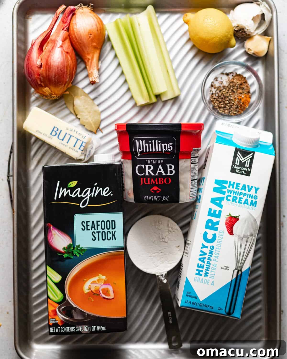 Classic She-Crab Soup: Southern Creamy Crab Recipe 2 ingredients to make she crab soup on a baking sheet - jumbo lump crab meat, seafood stock, heavy cream, butter, flour, seasonings, shallots, celery, lemon, garlic, and bay leaves.