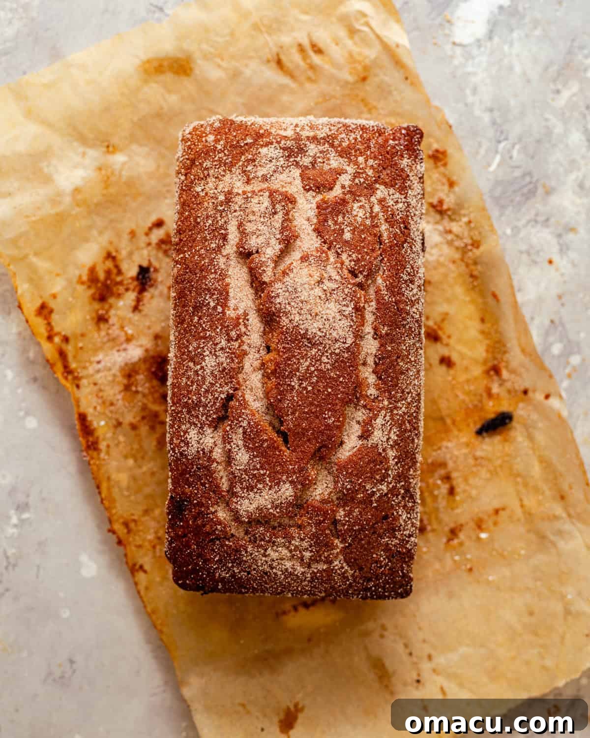 Warm Apple Cider Donut Loaf with Cinnamon Glaze 6 baked apple cider loaf on a piece of parchment paper covered in melted butter and sprinkled with cinnamon sugar.