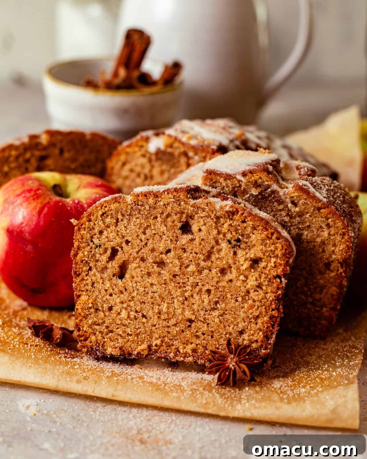 Warm Apple Cider Donut Loaf with Cinnamon Glaze 8 apple cider donut bread sliced on a piece of parchment paper placed next to an apple.